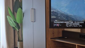 A modern living room with a large flat-screen TV on a wooden stand, a grey cabinet, a potted plant, and a small table with decorative items. - Modern, newly renovated Apartment in the heart of Ischgl (Ischgl)