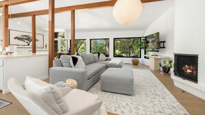 Un salon moderne avec un canapé d’angle gris, un fauteuil blanc et une cheminée.