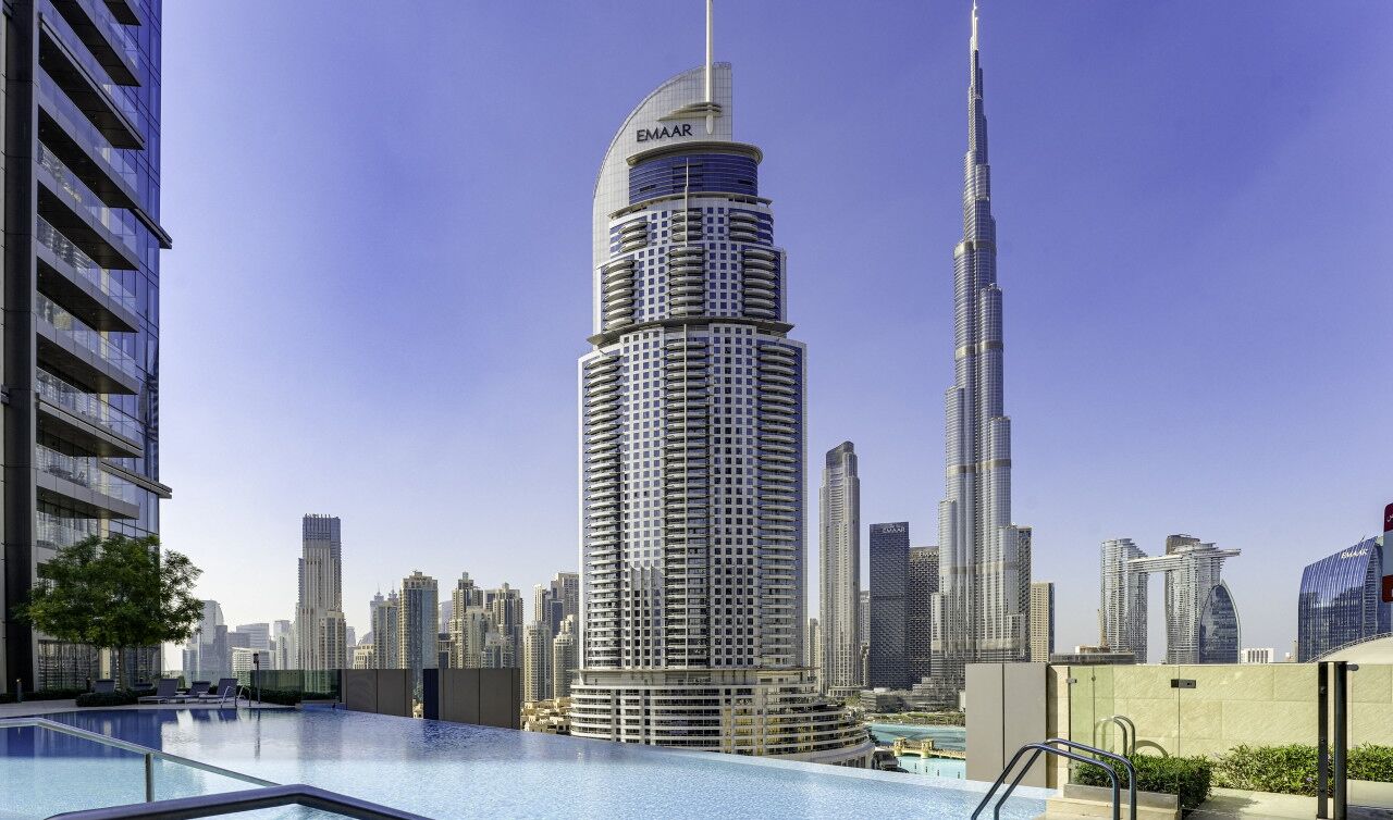 Un hotel moderno con piscina, circondato da edifici alti e un cielo sereno.