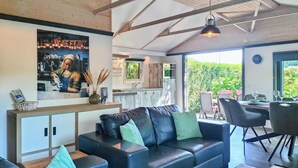 A modern living room with a leather sofa, a dining area with chairs, a kitchen with a wooden countertop, and a large window overlooking greenery. - 3 bedroom amazing home in Heinkenszand (Heinkenszand)