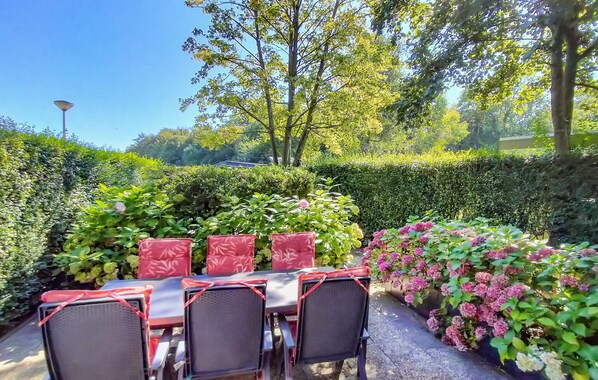 An outdoor dining area with a table and chairs, surrounded by lush greenery and flowering plants.