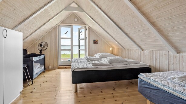 A cozy attic bedroom with a wooden sloped ceiling, a bed, a desk with a chair, and a window offering a view of the outdoors. - Lovely home in Fur with sauna (Fur)