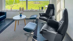 A modern living room with a large window overlooking a grassy area and the sea. There are two black leather chairs, a small round table, and a blue vase with flowers. - Lovely home in Fur with sauna (Fur)
