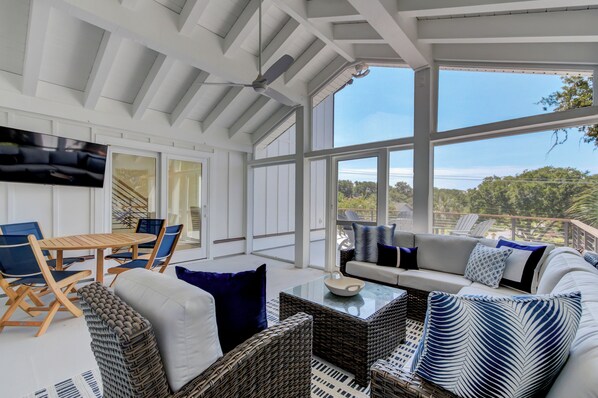 A spacious sunroom with a large sliding glass door, wicker furniture, a flat-screen TV, and a ceiling fan.