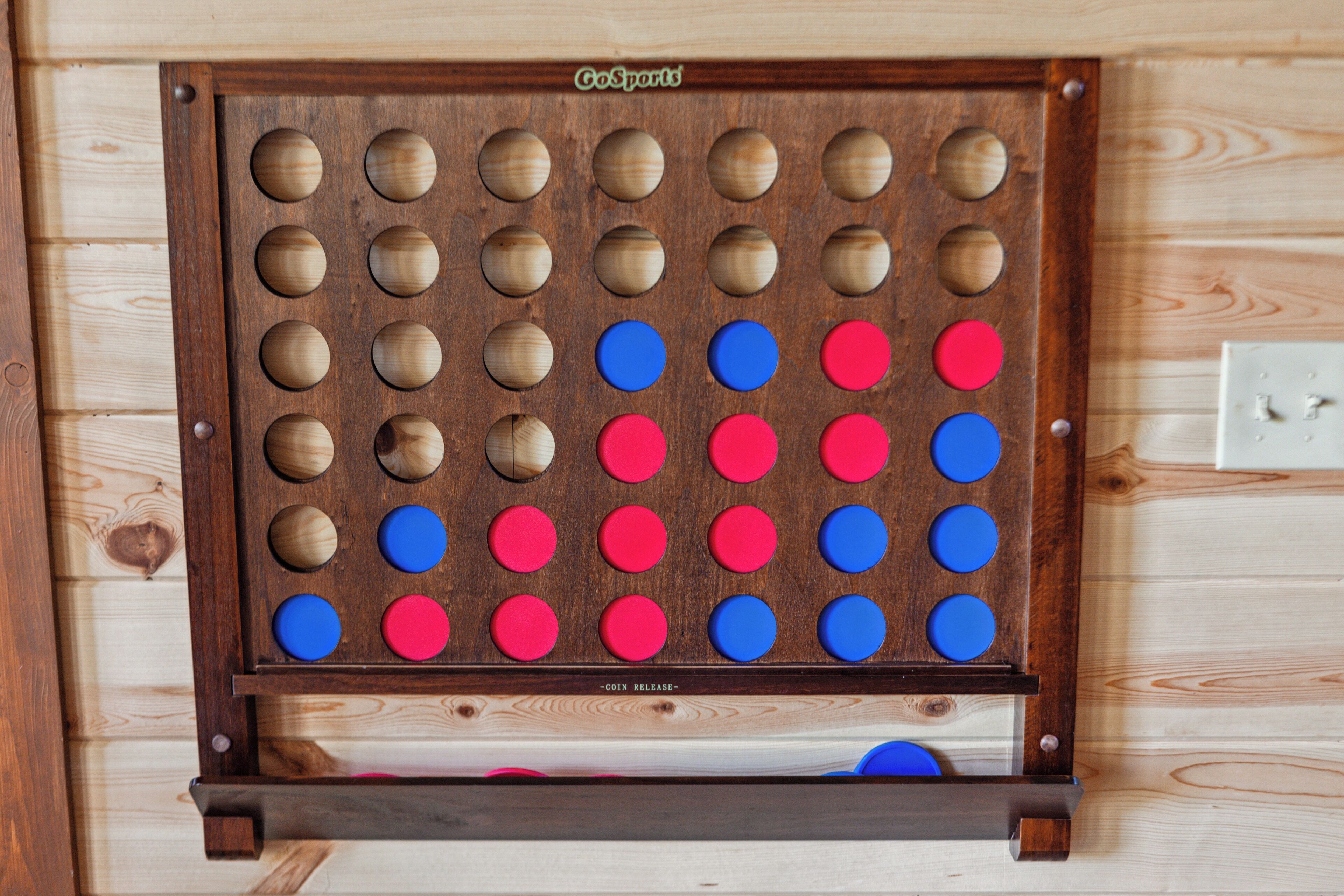 A wooden board with circular holes arranged in a grid, some filled with red and blue tokens.