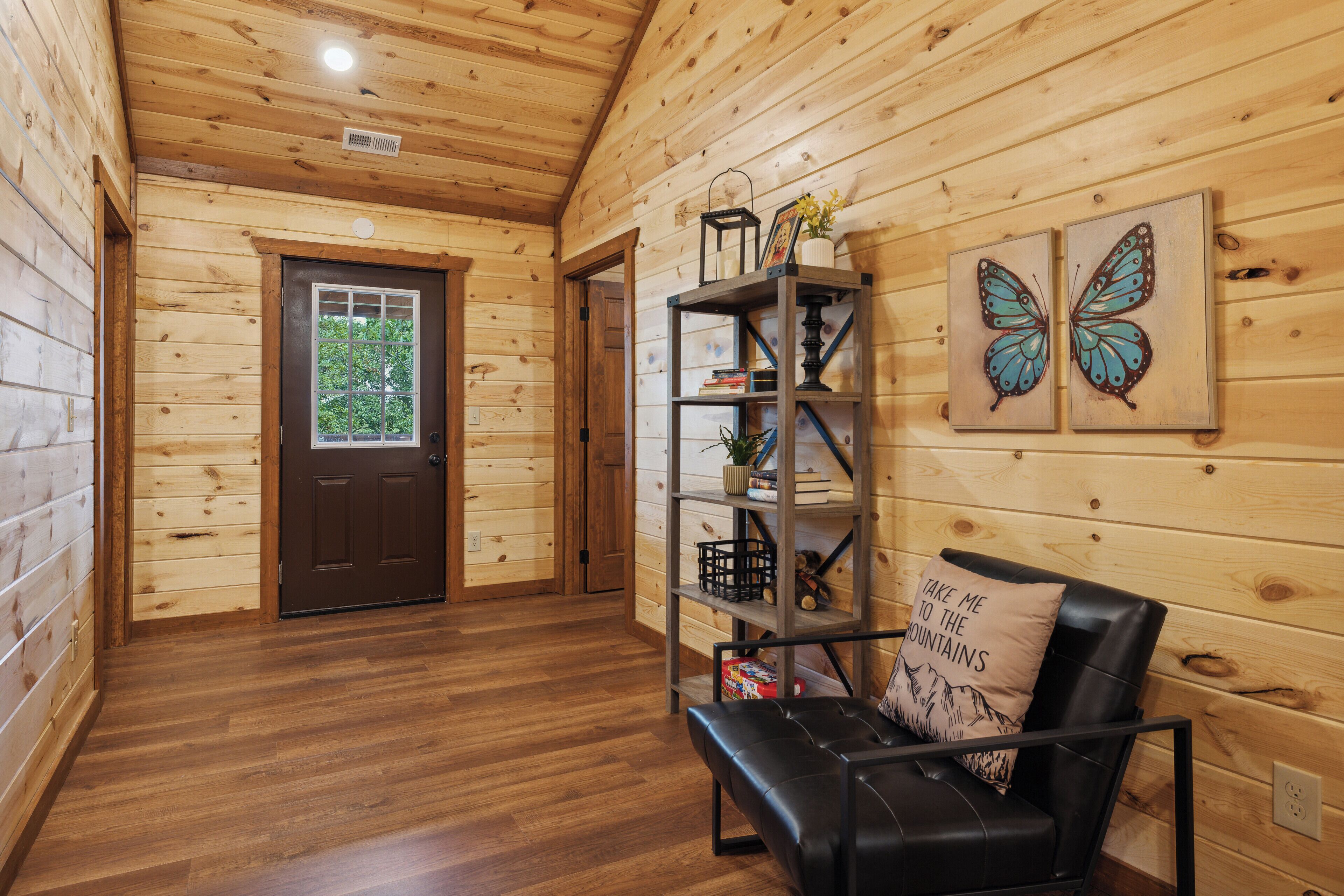 A wooden interior with a black leather sofa, a bookshelf, and two butterfly wall art pieces.