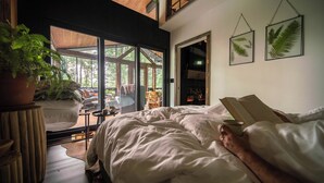 Ein Schlafzimmer mit einem großen Bett, einem Topfpflanzen und Blick auf eine Terrasse und Bäume.
