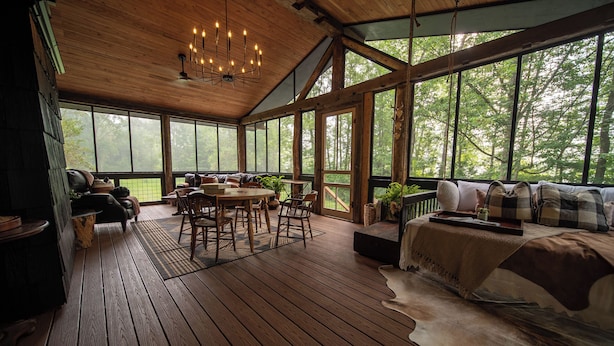 Eine geräumige Holzterrasse mit Essbereich, einer Couch und einem großen Fenster mit Blick auf Bäume.
