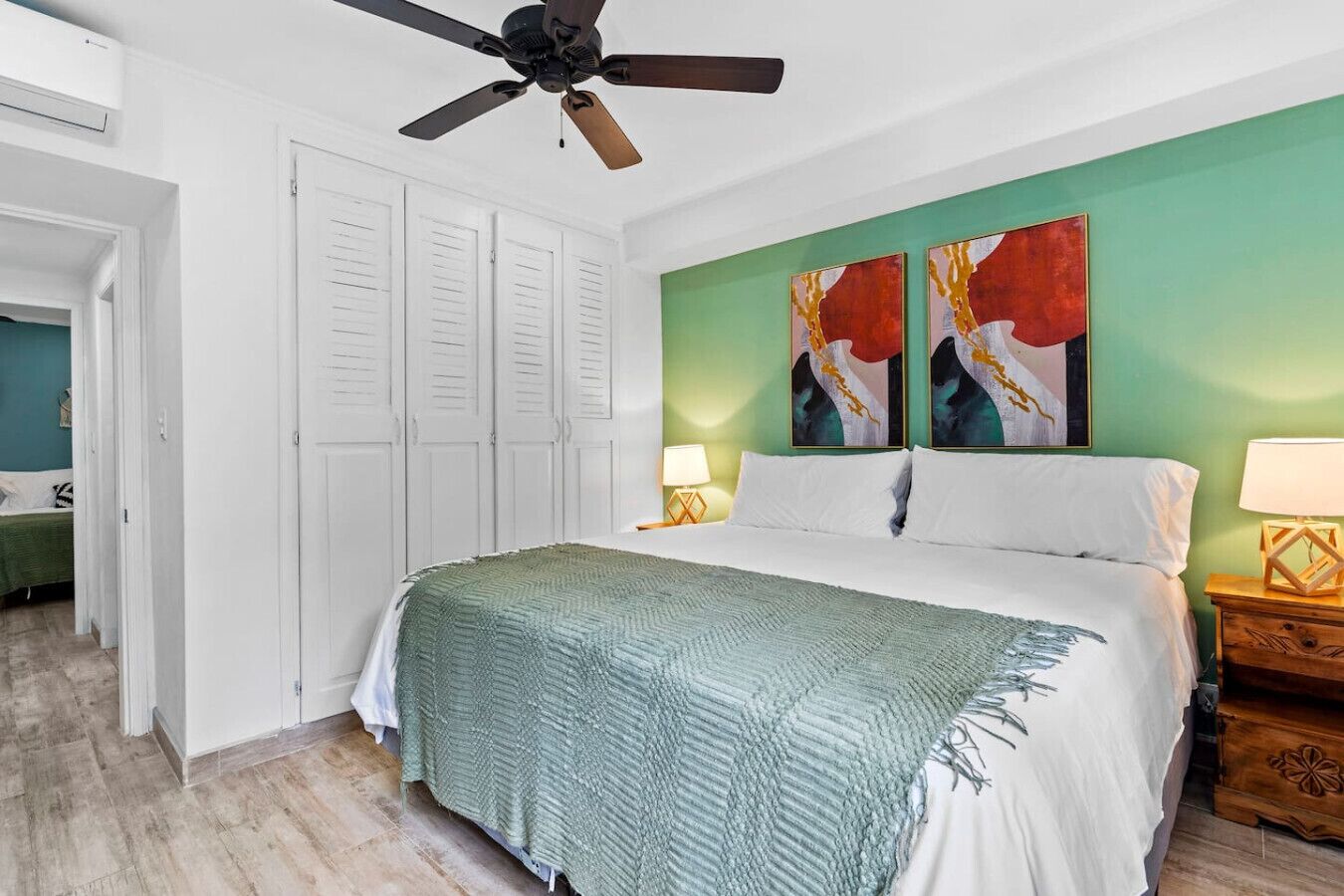 A bedroom with a bed, a ceiling fan, a nightstand, and two paintings on the wall.