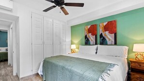 A bedroom with a bed, a ceiling fan, a nightstand, and two paintings on the wall. - Classy Condo in the heart of town (Tamarindo)