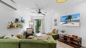 A modern living room with green sofas, a ceiling fan, a TV, and a beach-themed painting. - Classy Condo in the heart of town (Tamarindo)