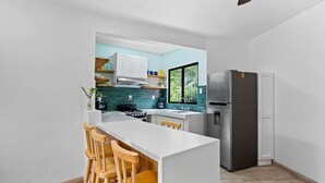A modern kitchen with a central island, wooden bar stools, a built-in stove, and a refrigerator. - Classy Condo in the heart of town (Tamarindo)