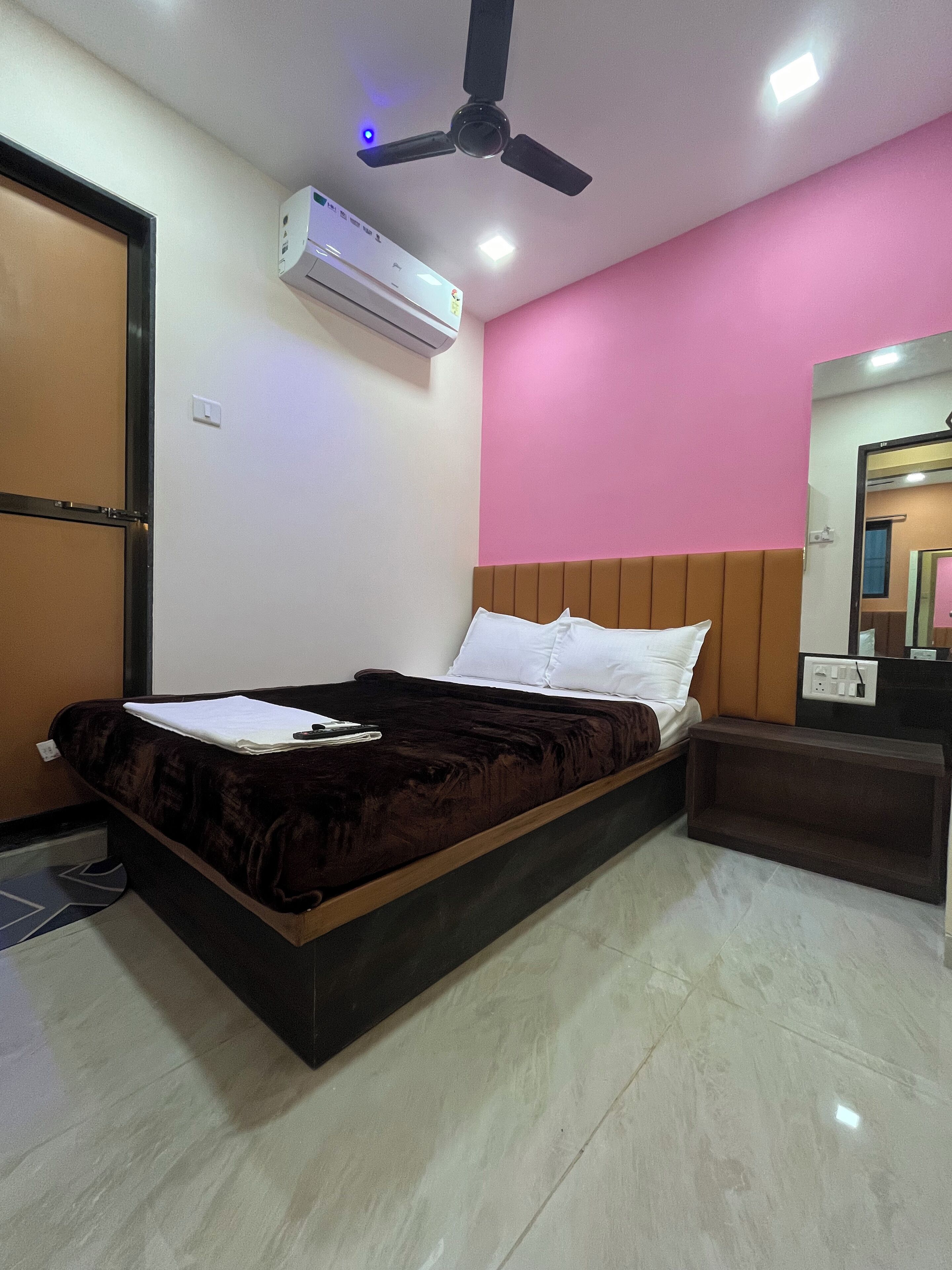 A bedroom with a bed, a ceiling fan, an air conditioner, a bedside table, and a mirror.