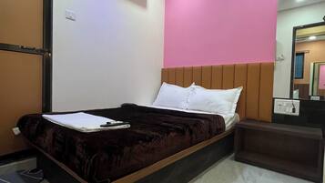 A bedroom with a bed, a ceiling fan, an air conditioner, a bedside table, and a mirror.