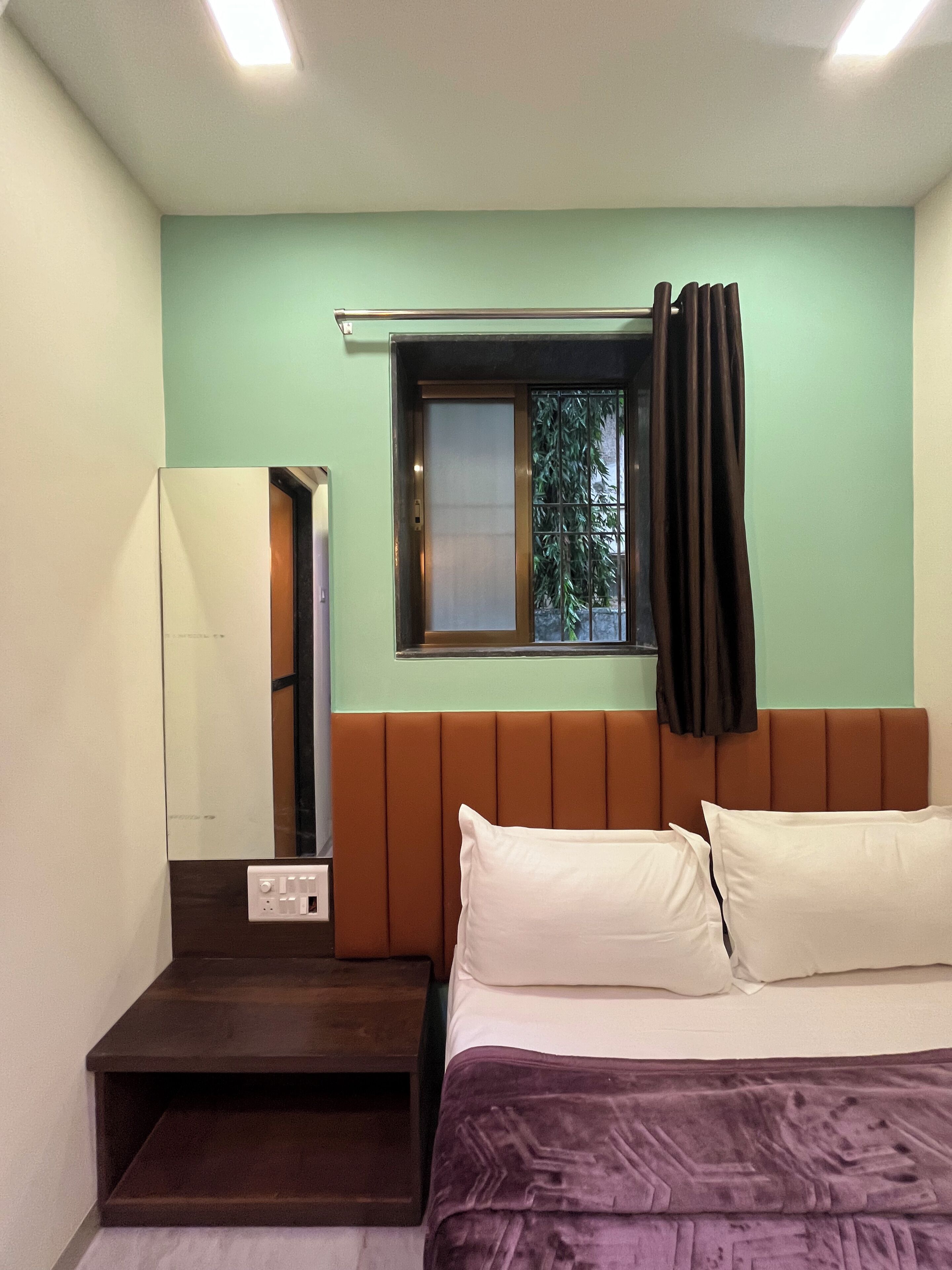 A bedroom with a bed, a window with curtains, a nightstand, and a mirror.