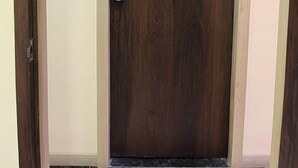 A closed wooden door with a silver handle and a light switch on the wall to its left. - Parel Residency (Mumbai)