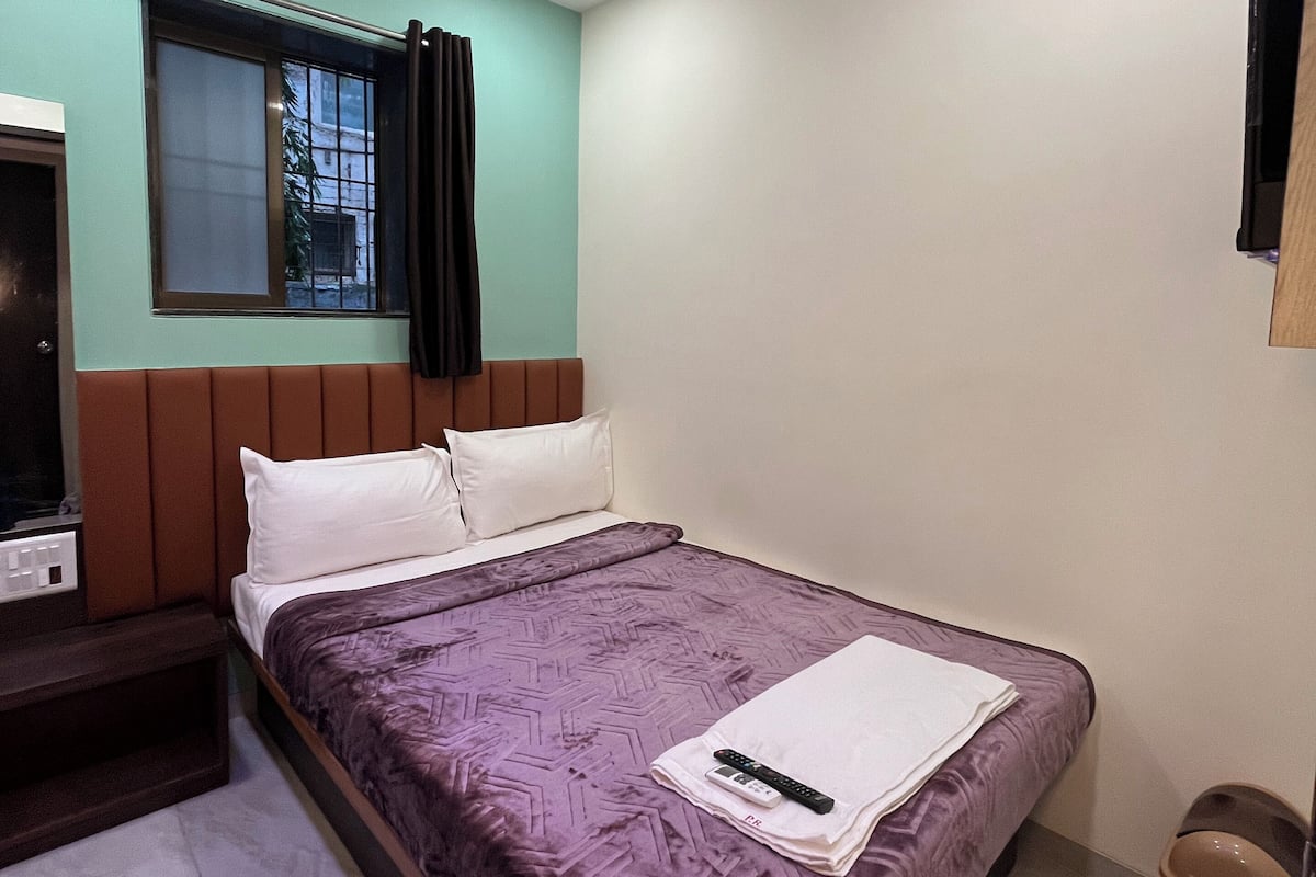 Una camera da letto con un letto, una ventola a soffitto, una finestra con tende, una TV e un cestino.