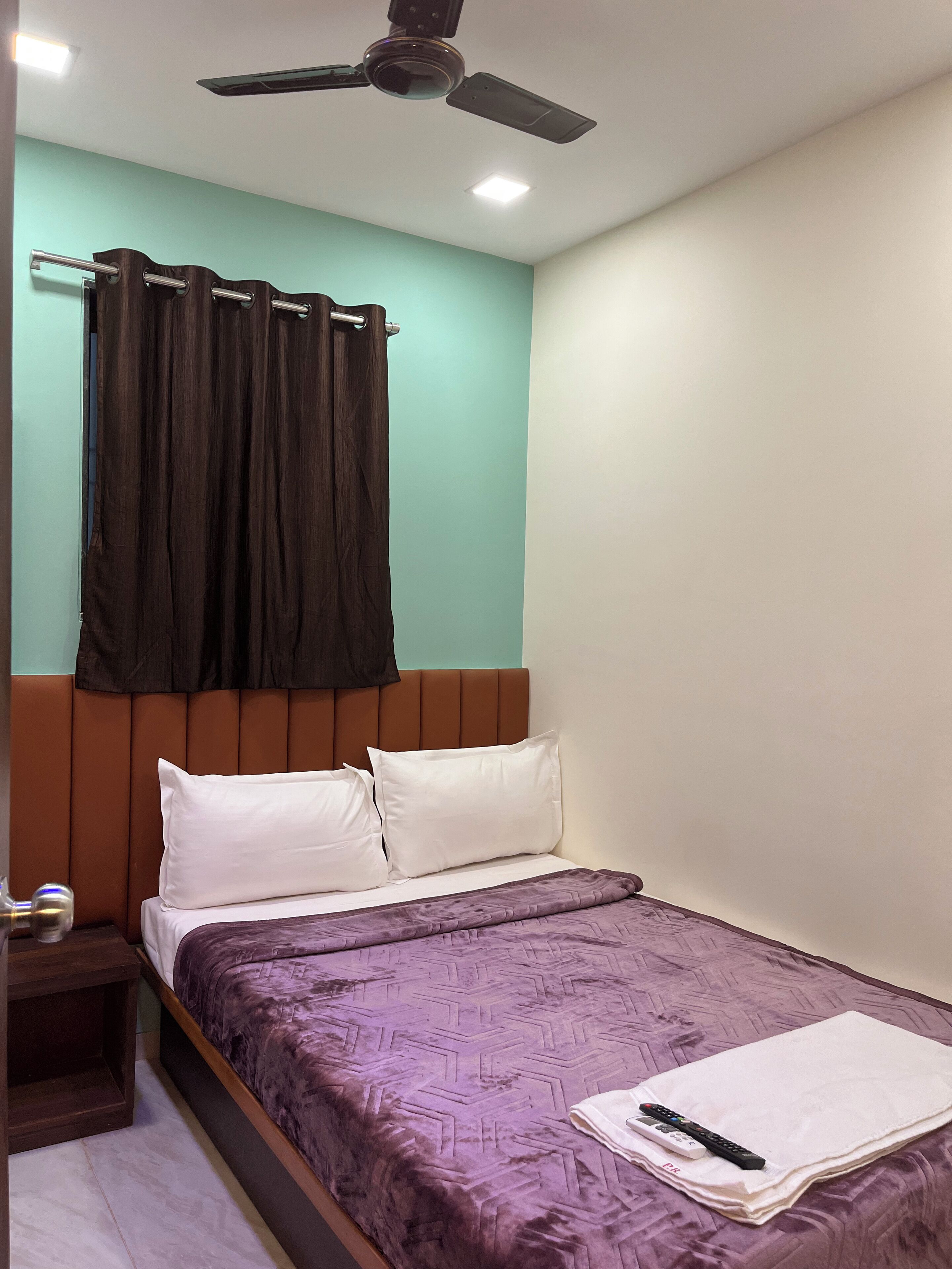 Un dormitorio con cama, ventilador de techo, mesita de noche y ventana con cortinas.