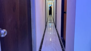 A hallway with a marble floor, a wooden door on the left, and a light switch on the wall. - Parel Residency (Mumbai)