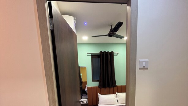 A hotel room with a bed, a ceiling fan, a window with curtains, and a door leading to another room. - Parel Residency (Mumbai)