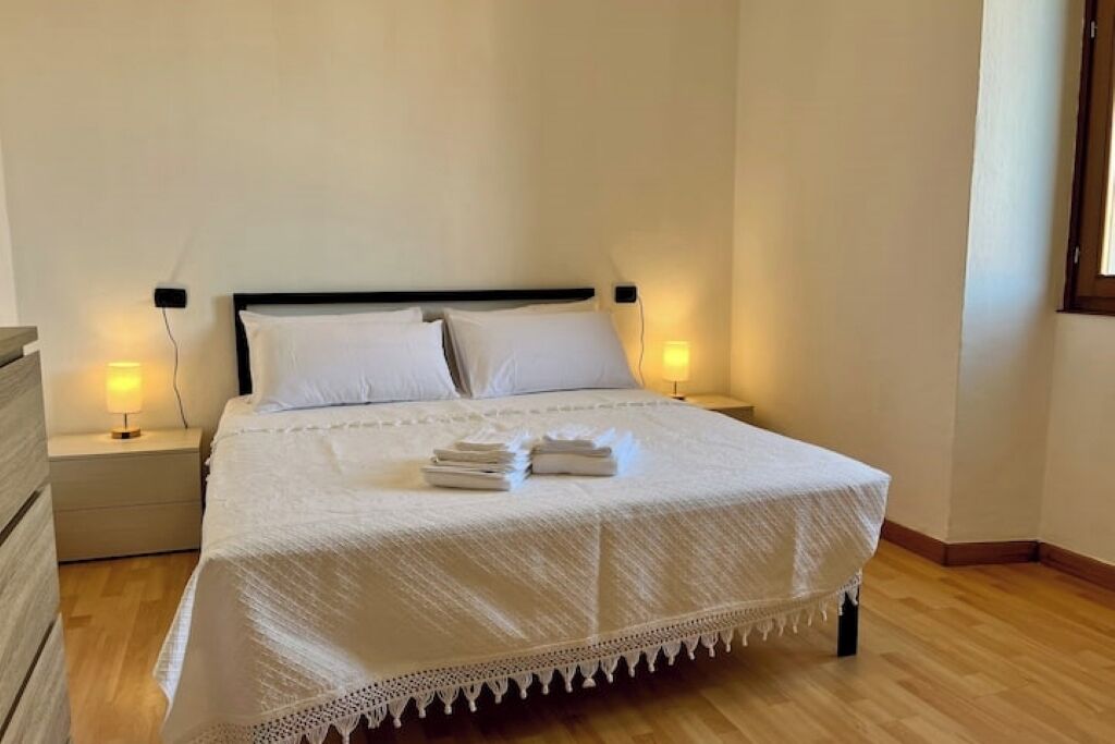 A neatly made bed with a white bedspread and pillows, two bedside lamps, and a wooden floor.