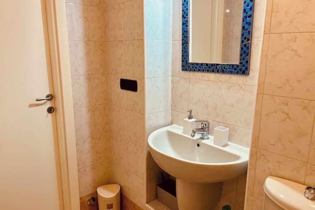 A bathroom with a white sink, a mirror with a blue frame, and a toilet.