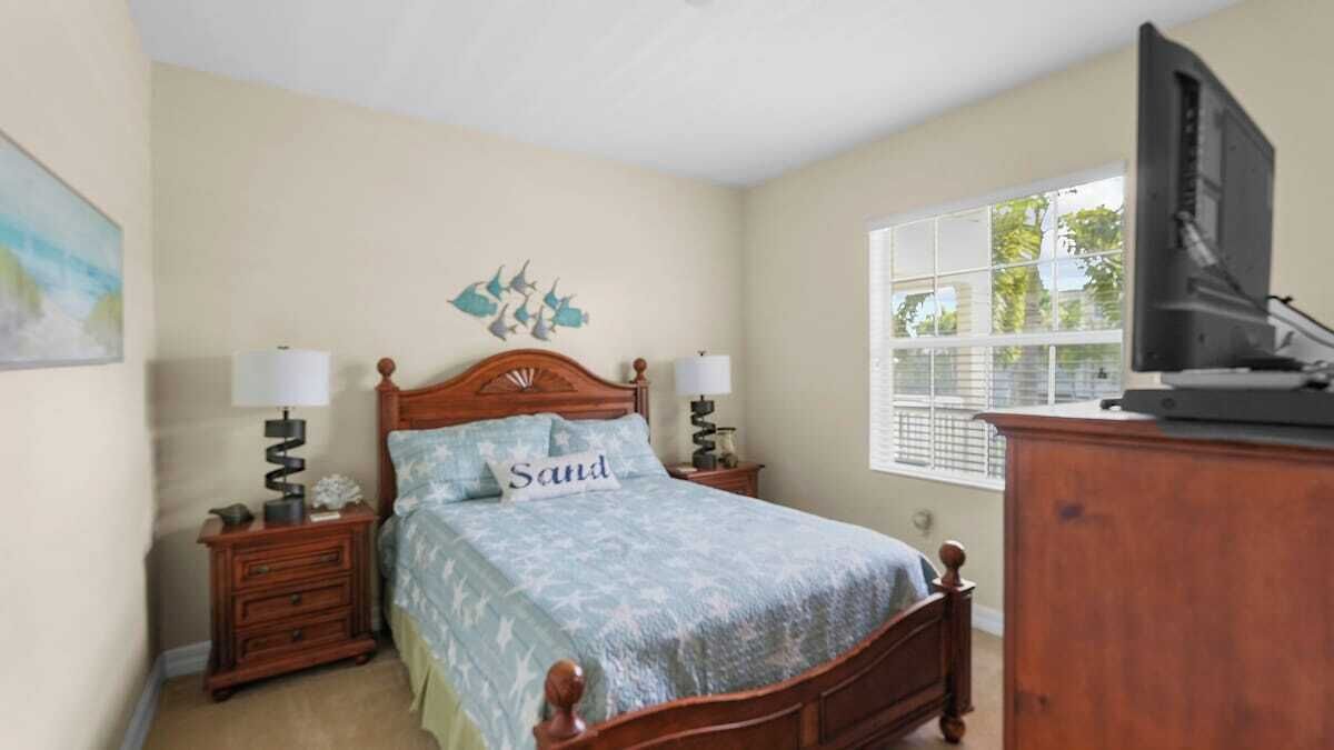 A bedroom with a wooden bed, two bedside tables, a television, and a window with blinds.