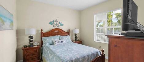 A bedroom with a wooden bed, two bedside tables, a television, and a window with blinds.