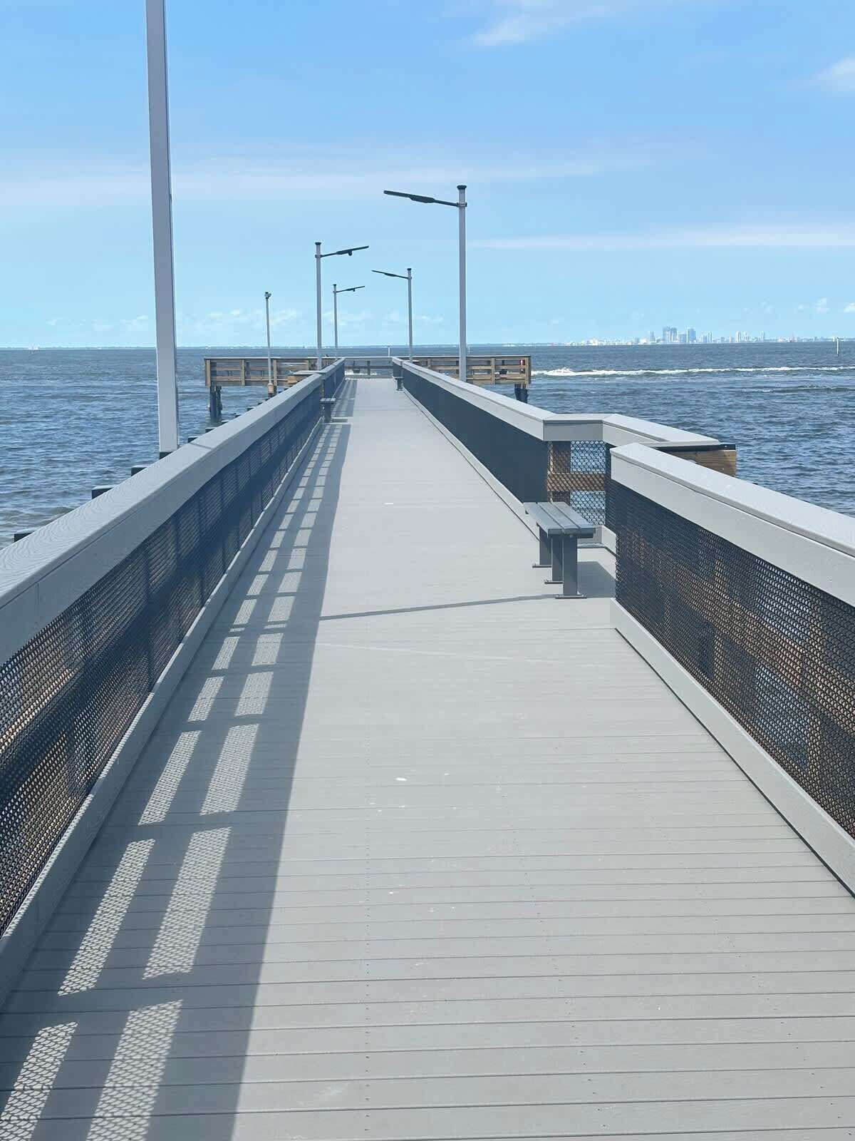 A long, straight pier extending into the water with a clear view of the city skyline in the distance.