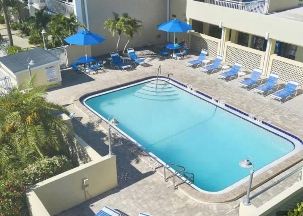 Une piscine rectangulaire bordée de carreaux, entourée de chaises longues et d’ombrelles bleues.