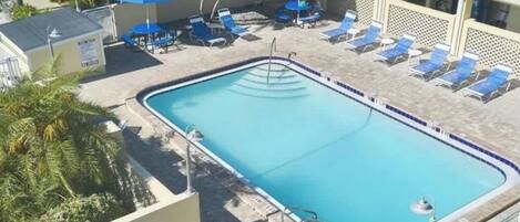 Une piscine rectangulaire bordée de carreaux, entourée de chaises longues et d’ombrelles bleues.
