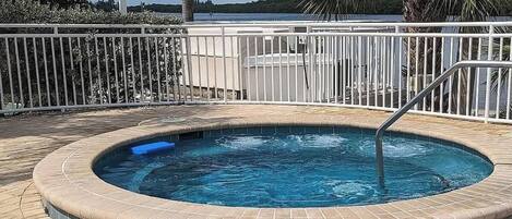 A hot tub with a tiled edge, surrounded by a white metal fence, and a view of a body of water in the background.