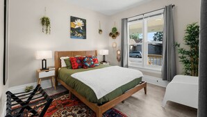 A bedroom with a bed, bedside tables, a window with curtains, a view of the outside, and a hanging plant. - Palacio Mexicano (Detroit)
