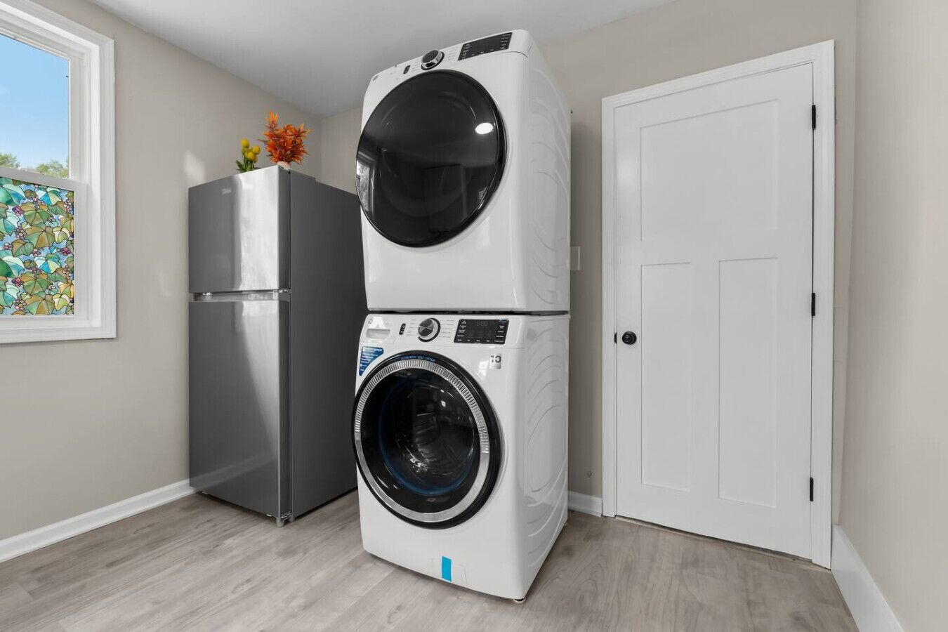 A laundry room with a stacked washer and dryer, a refrigerator, and a door.