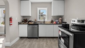 A modern kitchen with grey cabinets, a dishwasher, a stove, and a window above the sink. - Palacio Mexicano (Detroit)