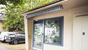 A building with a glass door entrance, a parking area with cars, and a tree in the background.