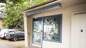 Ein Gebäude mit Glastür, ein Parkplatz mit Autos und ein Baum im Hintergrund.