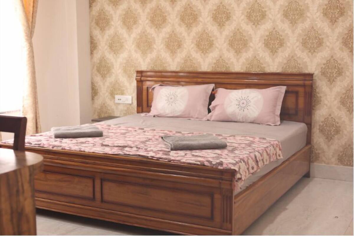 Un lit bien fait, avec une tête de lit en bois, une couvre-lit à motifs et deux oreillers.
