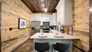 Una cocina moderna con paredes de madera, armarios blancos, una isla central con taburetes altos y una lámpara colgante.