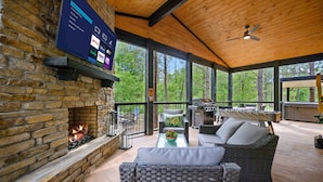 Un espacio al aire libre cubierto con una chimenea de piedra, muebles de mimbre y una pantalla grande que muestra servicios de streaming.