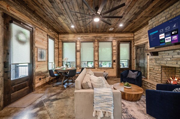 A wooden interior with a ceiling fan, a fireplace, a TV displaying streaming services, and a dining area.