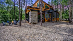 Una cabaña moderna con base de piedra, amplias ventanas y una terraza con mobiliario exterior.