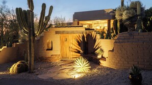 Edificio in stile desertico con una porta in legno, circondato da cactus e piante grasse.