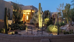 Un giardino desertico con diversi cactus e un edificio con una porta illuminata dall'interno.
