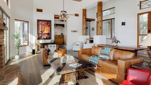 Un ampio soggiorno con un grande tavolino in legno, divani in pelle e una poltrona rossa. Si nota un camino, un quadro di grandi dimensioni e un'area pranzo sullo sfondo.