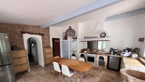A compact kitchen with a dining table, white chairs, a built-in oven, and a dishwasher. - Charming provençal farmhouse with swimming pool, in the countryside by the river (Le Thoronet)