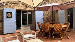 An outdoor patio with a round wooden table and chairs, a white folding chair, and a large umbrella. - Charming provençal farmhouse with swimming pool, in the countryside by the river (Le Thoronet)