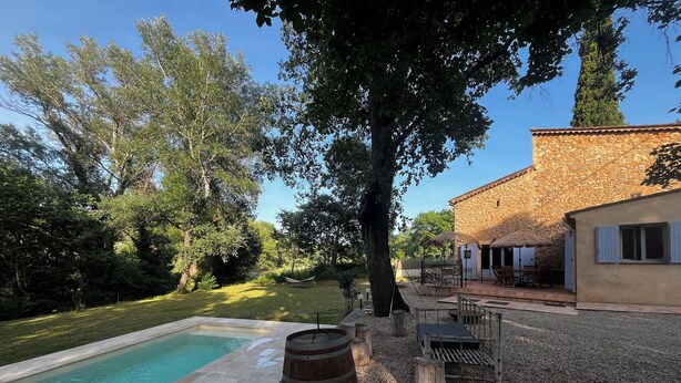 A pool with a stone deck, a wooden barrel, and a stone building with outdoor seating. - Charming provençal farmhouse with swimming pool, in the countryside by the river (Le Thoronet)