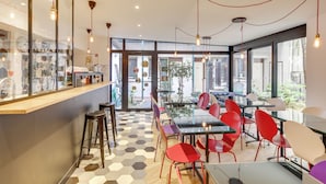 Un café moderne avec un comptoir en verre, des chaises rouges et blanches, et un sol à motifs hexagonaux.