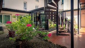 Un espace extérieur moderne doté d’une structure vitrée, d’un escalier en bois et d’un jardin agrémenté de fleurs roses.